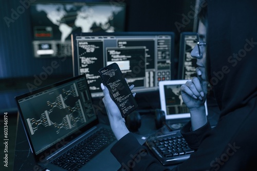Holding smartphone with code. Young professional female hacker is indoors by computer with lot of information on displays