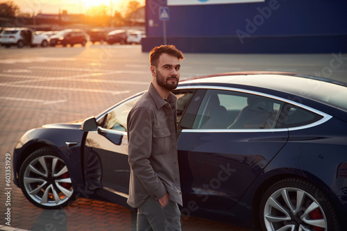 Gorgeous stylish man is standing near his electric car outdoors © standret