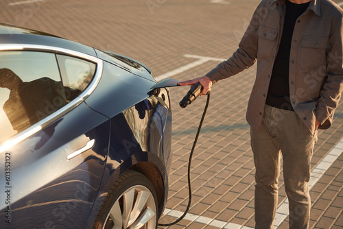 Beautiful yellow sunlight. Man is standing near his electric car outdoors