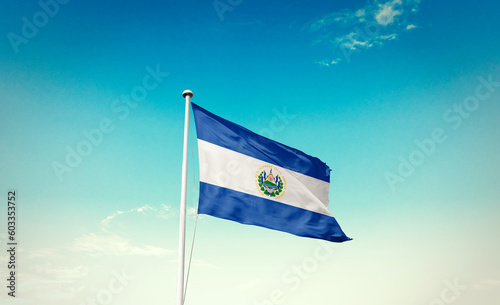 Waving Flag of El Salvador in Blue Sky. The symbol of the state on wavy cotton fabric.