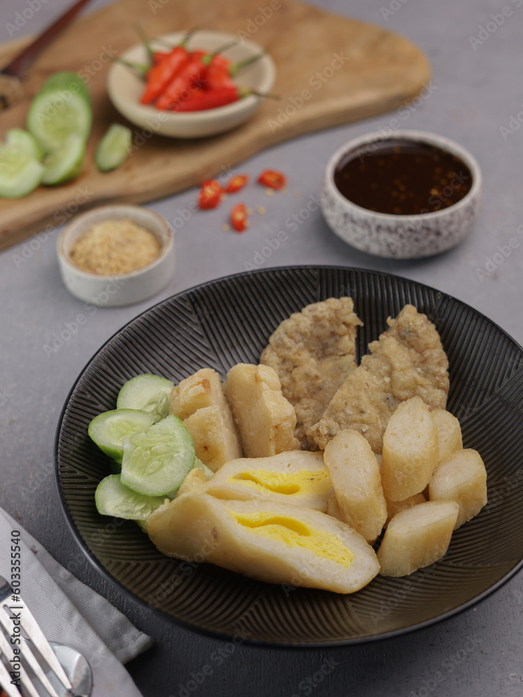 Pempek Palembang, an Indonesian traditional cuisine made from fish cake served with sweet spicy sour sauce and diced cucumber. Piled on white plate on the table Pempek Palembang, an Indonesian traditional cuisine made from fish cake served with sweet spicy sour sauce and diced cucumber. Piled on white plate on the table