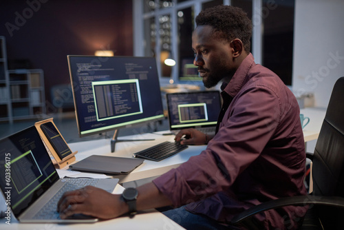 African American programmer concentrating on his online work on computers while working in office till late evening