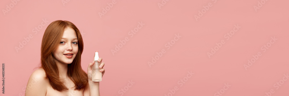 Young, beautiful, redhead girl with healthy, well-kept skin holding face toner against pink background. Concept of natural beauty, makeup, cosmetology, cosmetics, skin care. Banner. Copy space for ad Young, beautiful, redhead girl with healthy, well-kept skin holding face toner against pink background. Concept of natural beauty, makeup, cosmetology, cosmetics, skin care. Banner. Copy space for ad