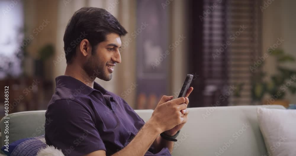 Indian Man Using Smartphone at Home: Engaging in Social Media, Discovering New Music, Learning New Skills through Online Courses, and Embracing the Power of Technology. Medium Shot SLow motion