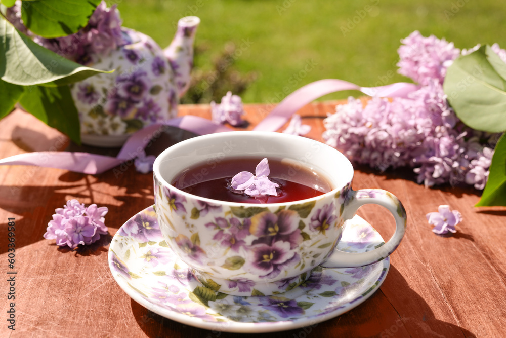 Spring composition with a purple cup with flowers on it,  teapot and lilac flowers on light background.  Tea drinking. Menu, greeting card. 
Spring time. The concept of 'Good morning'