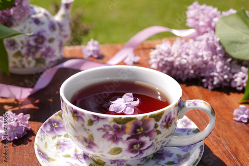 Spring composition with a purple cup with flowers on it, teapot and lilac flowers on light background. Tea drinking. Menu, greeting card. Spring time. The concept of 'Good morning'