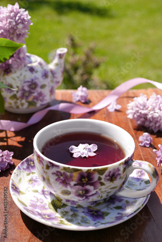 Spring composition with a purple cup with flowers on it, teapot and lilac flowers on light background. Close up. Tea drinking. Menu, greeting card. Spring time. The concept of 'Good morning' 