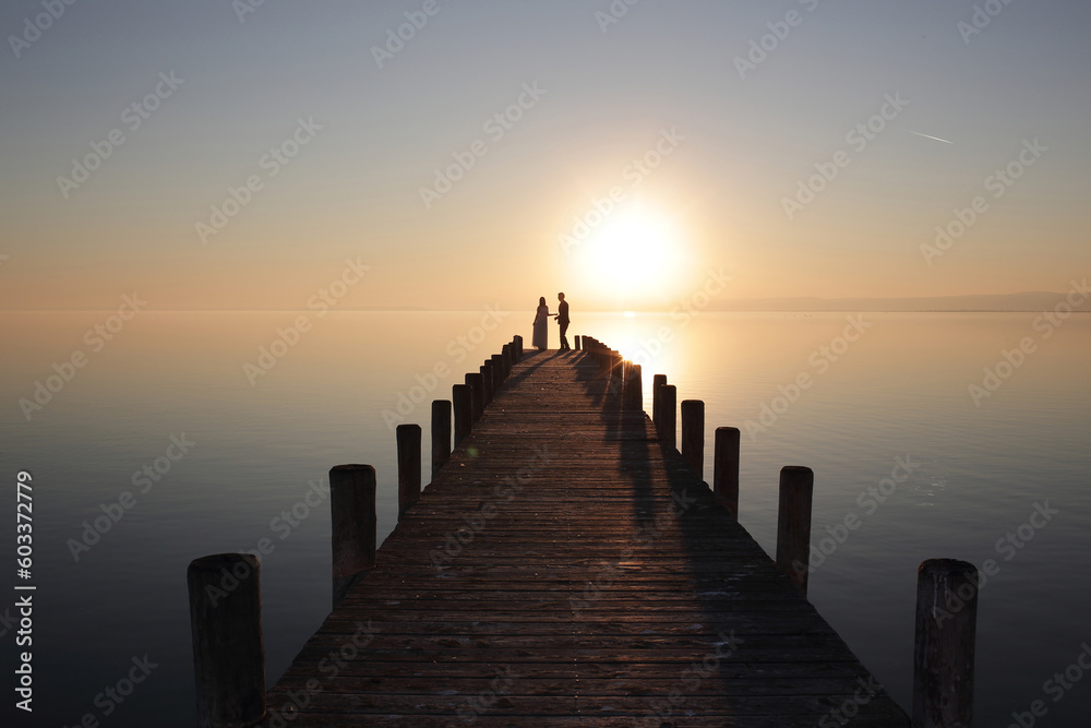 Groom and bride standing on wooden stage holding hands at sunset