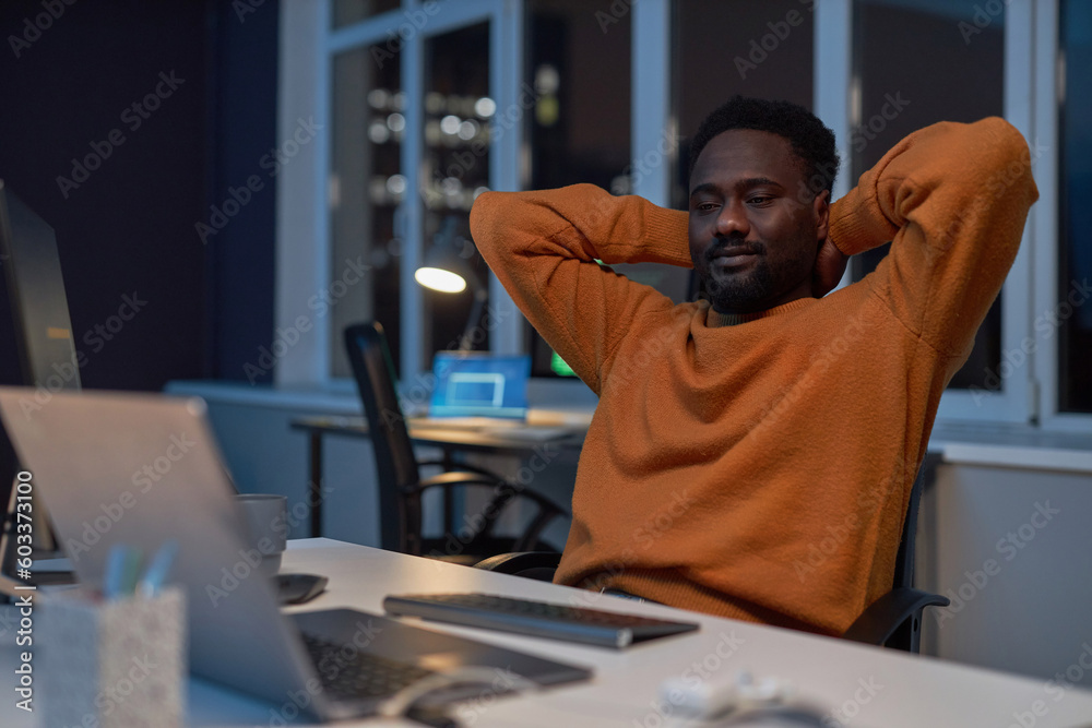 African American developer resting at hs workplace after work in dark office African American developer resting at hs workplace after work in dark office