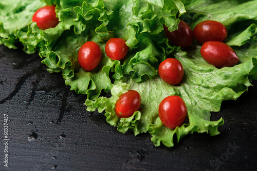 fresh green lettuce leaves and small red cherry cocktail tomatoes on black wooden background