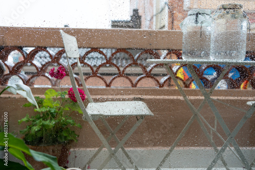 Balcony and roofs on a rainy day in Barcelona, white metal table, flowers, two glass jars with water on the balcony to remove the chlorine in the sun. Outside 