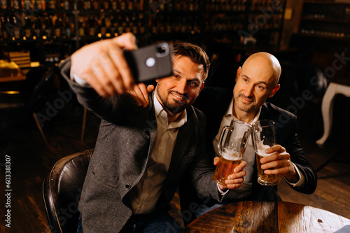 friends drinking beer and taking selfie with smartphone in bar or pub. male friendship - happy.