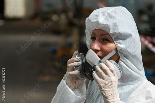 Caucasian woman workers wearing PPE protective clothing and gas masks, goggles, holding old petrol tanks.