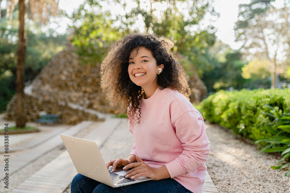 pretty curly young woman sitting in park working on laptop remote job pretty curly young woman sitting in park working on laptop remote job
