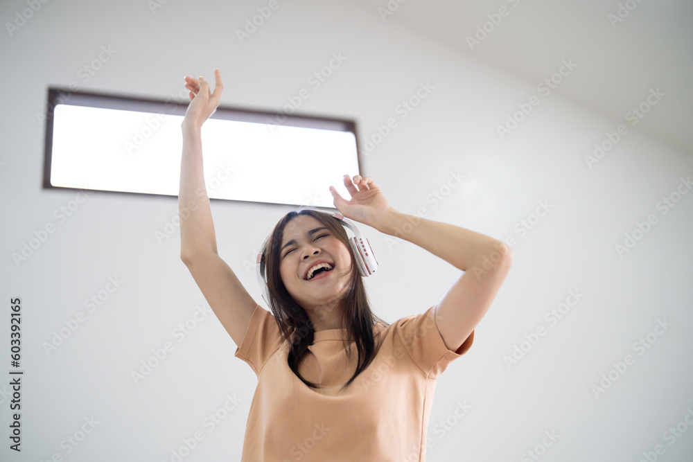 Happy Young Asian woman wearing headphone have fun and dancing listening to music relax in living room. beautiful joyful woman dancing in house