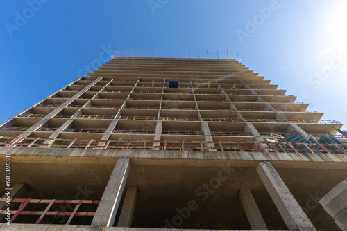 Close-up view from below of a multi-storey building under construction against a blue sky background.