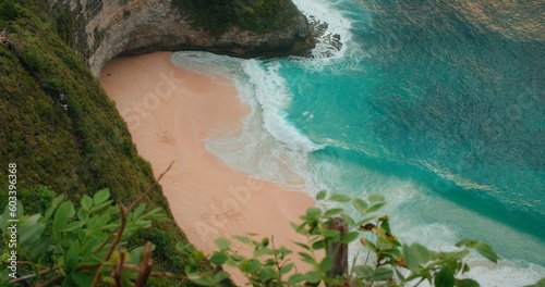 Turquoise ocean waves roll on golden sandy Kelingking beach at sunset in Bali Nusa Penida Indonesia. Pristine tropical landscape in slow-motion.