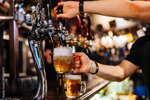 man bartender hand at beer tap pouring beer in glass in bar or pub