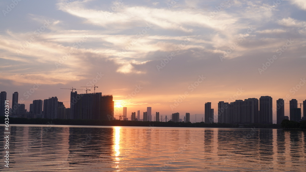 The beautiful sunset view with the buildings' silhouette and orange color sky mirrored in the peaceful lake in the city