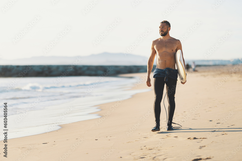 An athletic man surfer with naked torso standing on the seashore