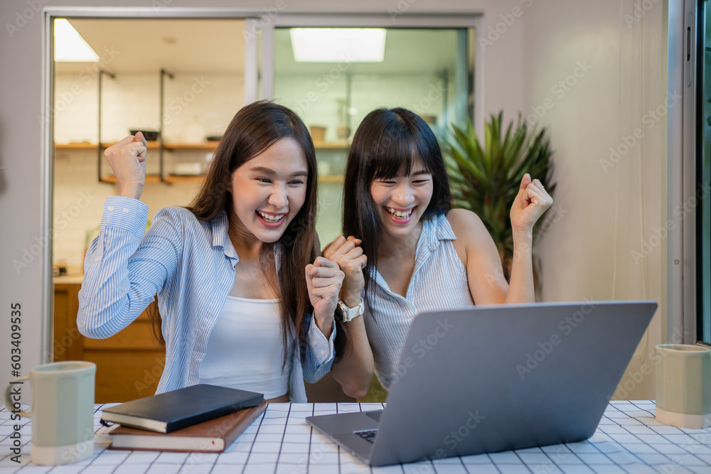 Cheerful girlfriends in had near face smiling while planning further work together and using laptop at home. Cheerful girlfriends in had near face smiling while planning further work together and using laptop at home.