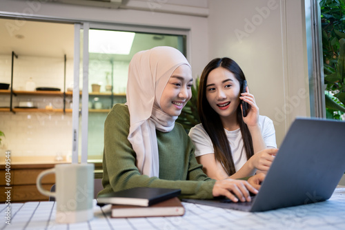 Cheerful girlfriends in had near face smiling while planning further work together and using laptop at home.