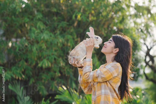 Woman lift up cute rabbit at her face level with sunset light and smile of love and happiness.