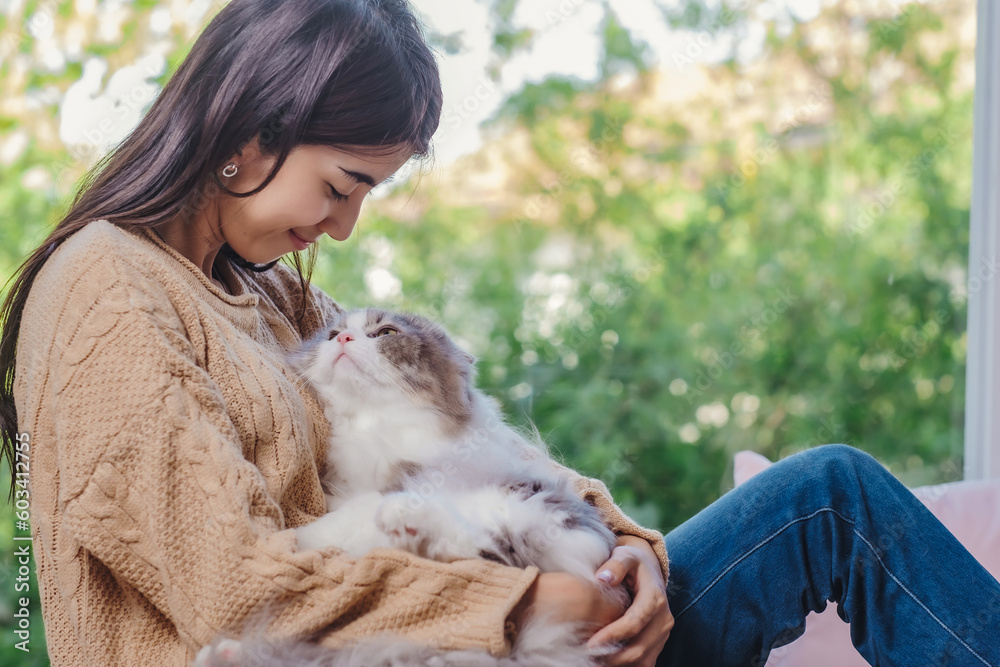 Woman with long hair in brown sweater and jean holding persain cat in her lap and embrassed him with love feelling, girl and cat looking each other with love and care emotion. Woman with long hair in brown sweater and jean holding persain cat in her lap and embrassed him with love feelling, girl and cat looking each other with love and care emotion.