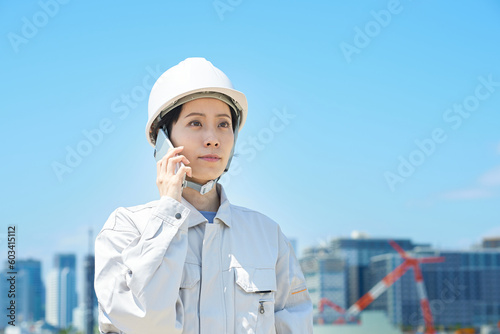 スマートフォンで通話する作業服姿の女性 © maru54