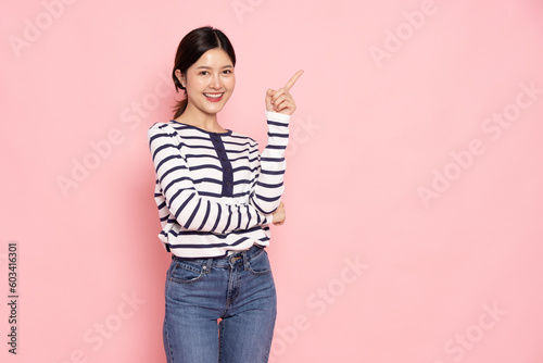 Young Asian woman smiling and pointing finger to empty copy space isolated on pink background