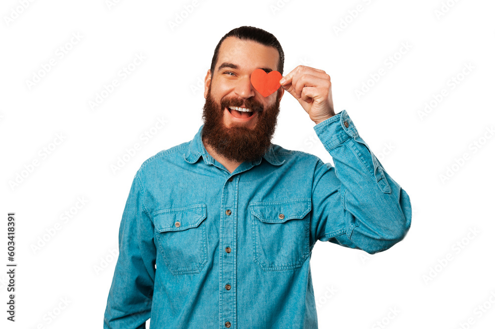 Fototapeta premium Wide smiling bearded man wearing blue shirt is holding a heart shaped paper over his eye.