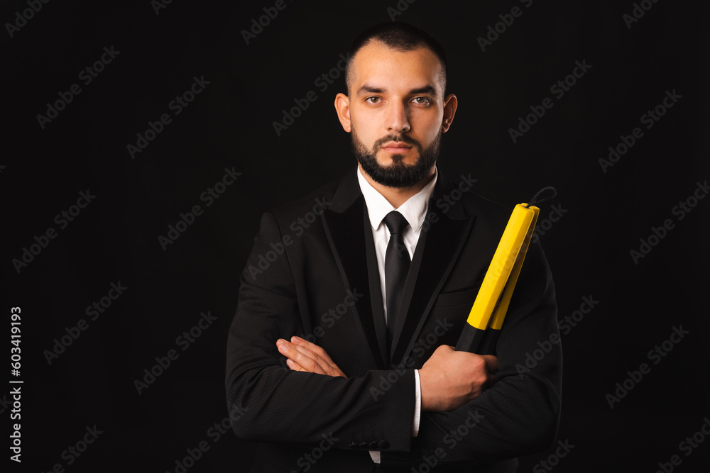 Front portrait of a strong serious man holding nunchaku and arms crossed. Studio shot over black background. Front portrait of a strong serious man holding nunchaku and arms crossed. Studio shot over black background.