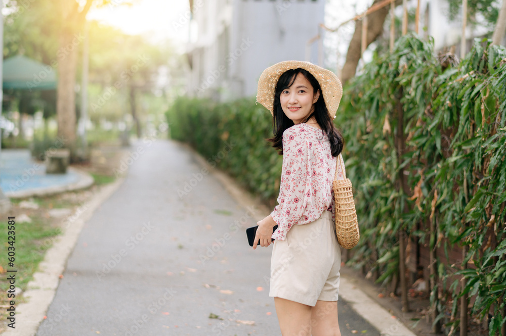 Obraz premium Portrait of asian young woman traveler with weaving hat and basket happy smile on green public park nature background. Journey trip lifestyle, world travel explorer or Asia summer tourism concept.