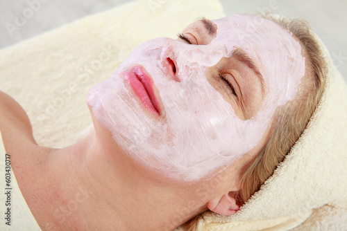 Spa Woman applying Facial Mask. Beauty Treatments. Close-up portrait of beautiful middle-aged woman with a towel on her head applying facial mask.
