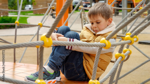Upset lonely boy sitting on the playground and embracing his legs. Child depression, problems with bullying, victim in school, emigration, criminal and poverty.