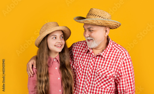 glad child with grandfather in straw hat on yellow background