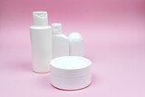 Set of white plastic cosmetic bottles, jar, and deodorant mock-up on the pink background. Skincare and body care concept, cosmetics, beauty industry.