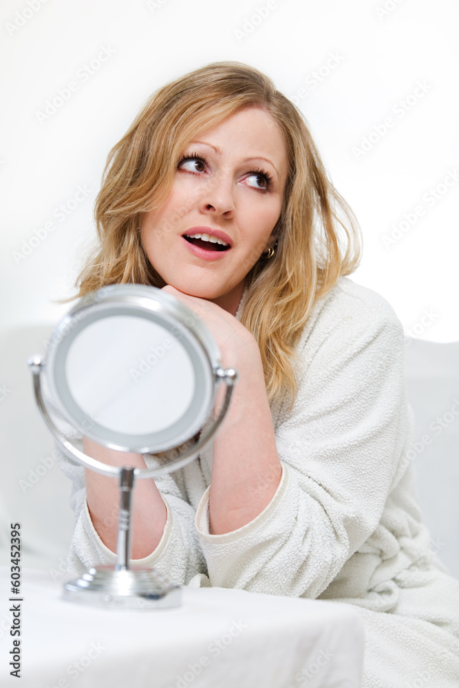 Attractive woman wearing white bathrobe sitting in front of a small round mirror Attractive woman wearing white bathrobe sitting in front of a small round mirror