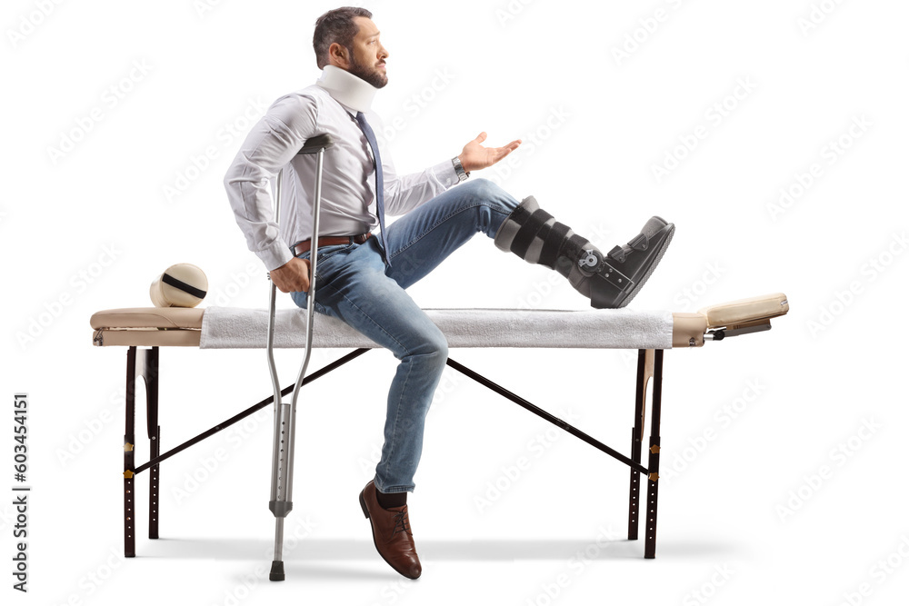Injured man with an orthopedic boot and neck collar sitting on a therapy table and gesturing with hand Injured man with an orthopedic boot and neck collar sitting on a therapy table and gesturing with hand