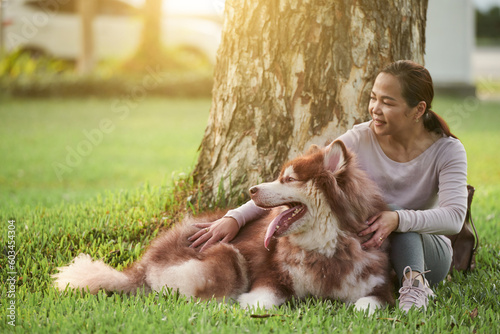 Happy woman sitting under tree in park and patting big dog