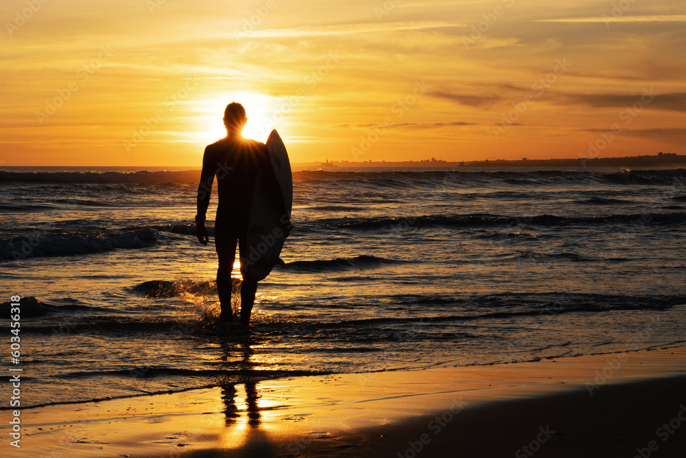 Dark silhouette of a man surfer holding surfboard at bright sunset