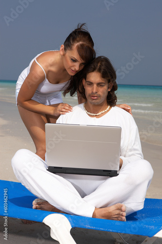 Romantic young couple working on laptop computer at the beach