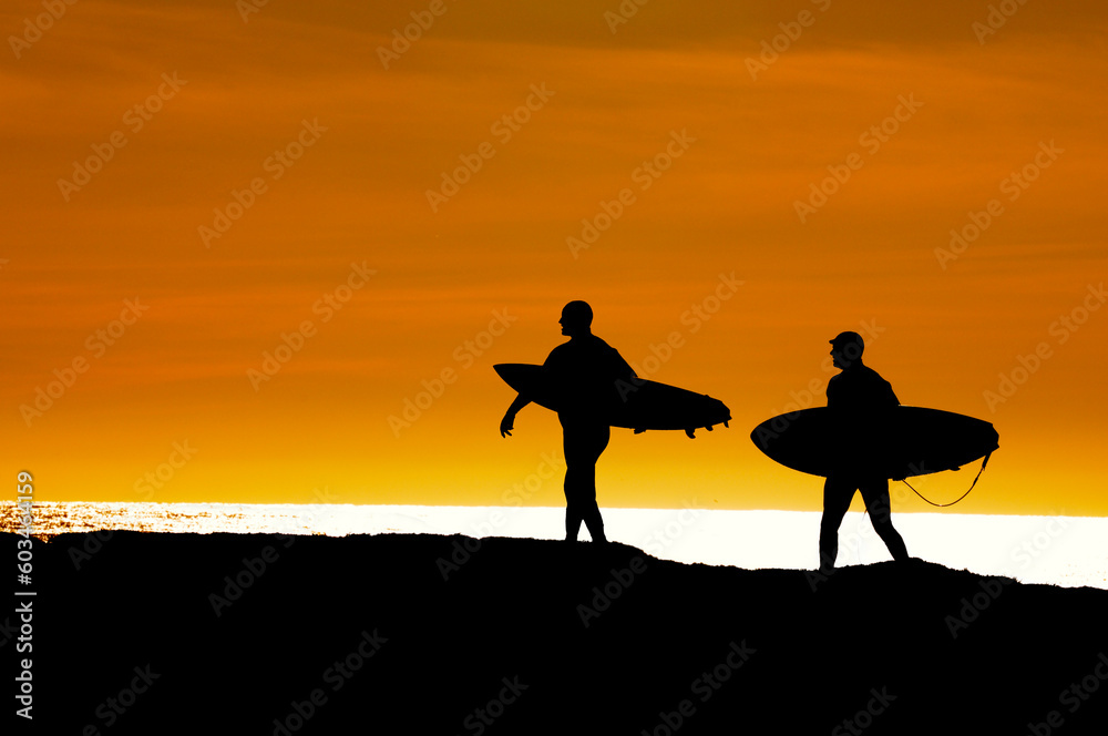 Pair of surfers heading along the cliffs at Santa Cruz for the last ride of the day as the sun sets Pair of surfers heading along the cliffs at Santa Cruz for the last ride of the day as the sun sets