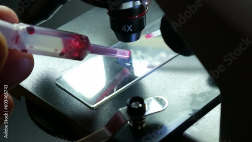 Close-up shot scientific laboratory microscope examining a drop of blood virus on a prepared sample slide. Education, science or medicine industry
