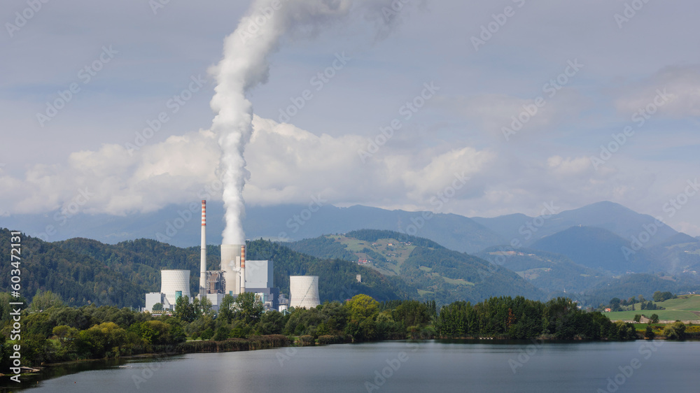 Smoking chimney at thermal power plant near lake and green nature.
