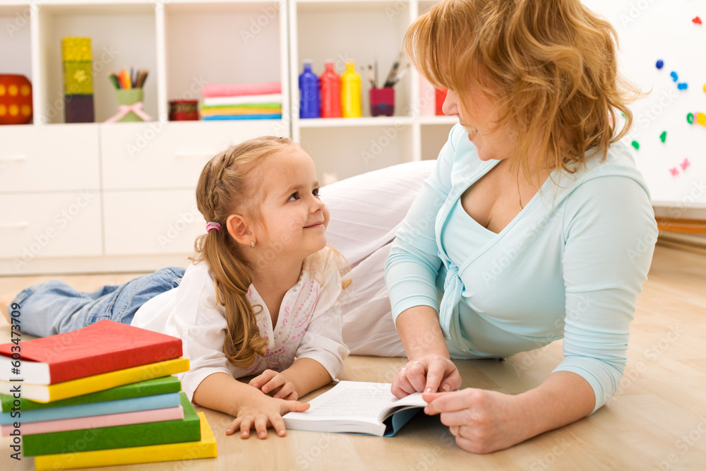 Fototapeta premium Story time with mom - little girl and woman reading laying on the floor