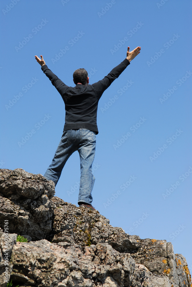 A man standing on a cliff with his arms raised to the blue sky A man standing on a cliff with his arms raised to the blue sky