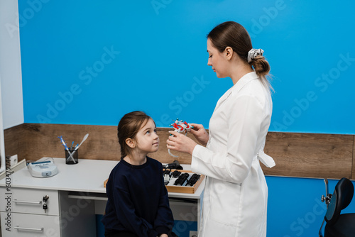Child examination with pediatric ophthalmologist for selection of trial glasses frame to examine eye visual system of child. Ophthalmologist selects lenses for trial frame of glasses.