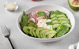 Salad with cucumbers, avocado, radishes and arugula, dressing with sour cream in white salad bowl