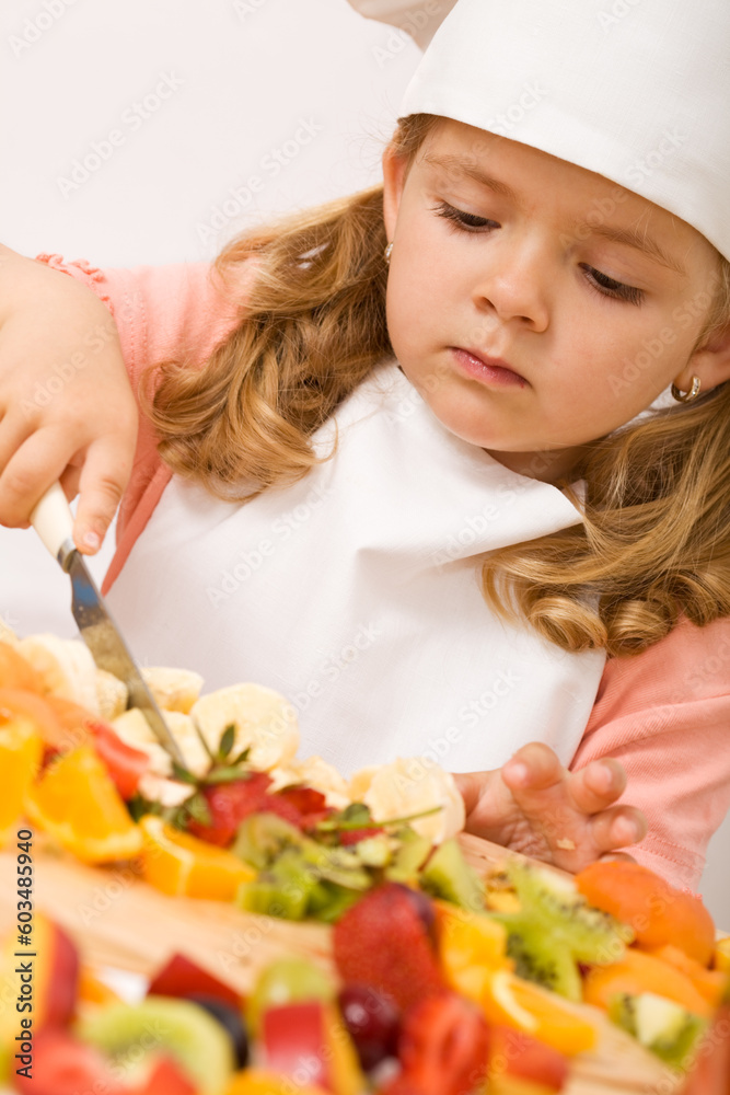 Little girl chef slicing lots of fruits for a nice fresh salad - closeup